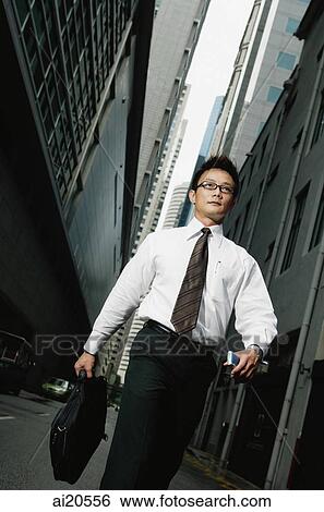 Businessman holding briefcase, walking, buildings around him View Large Photo Image Stock Photograph - Businessman holding briefcase, walking, buildings around him. Fotosearch
