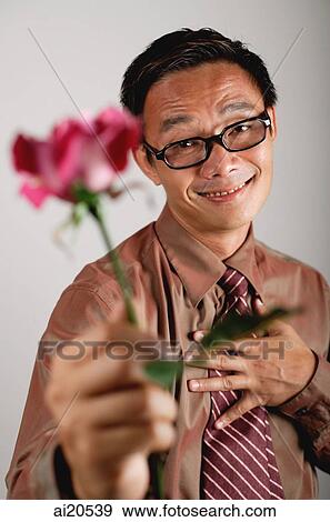 Businessman holding flower towards camera, hand on chest View Large Photo Image Stock Photo - Businessman holding flower towards camera, hand on chest. Fotosearch
