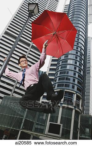 Businessman holding open umbrella, jumping around lamppost, buildings in the background View Large Photo Image Stock Photography - Businessman holding open umbrella, jumping around lamppost, buildings in the background. Fotosearch