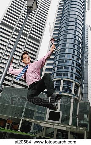 Businessman holding umbrella, jumping around lamppost, buildings in the background View Large Photo Image Picture - Businessman holding umbrella, jumping around lamppost, buildings in the background. Fotosearch