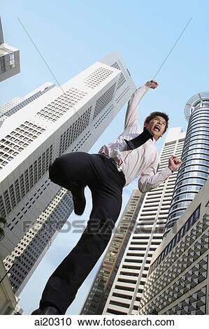 Stock Image - Businessman jumping in mid-air with arms raised, buildings in the background. Fotosearch