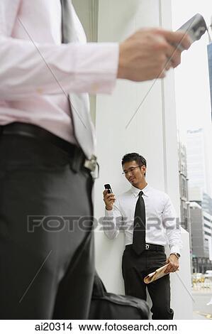 Picture - Businessman looking at mobile phone, person in the foreground. Fotosearch