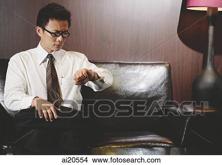 Picture - Businessman sitting on sofa, looking at his watch. Fotosearch