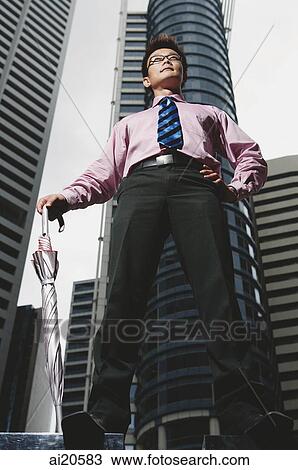 Businessman standing, holding umbrella, buildings in the background View Large Photo Image Stock Image - Businessman standing, holding umbrella, buildings in the background. Fotosearch