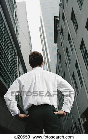 Businessman standing with hands on hips, surrounded by buildings, rearview View Large Photo Image Stock Photo - Businessman standing with hands on hips, surrounded by buildings, rearview. Fotosearch