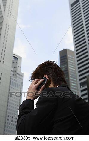 Businessman using mobile phone, buildings behind him View Large Photo Image Stock Photography - Businessman using mobile phone, buildings behind him. Fotosearch