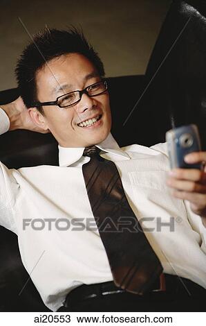 Businessman with hand behind head, looking at mobile phone View Large Photo Image Stock Image - Businessman with hand behind head, looking at mobile phone. Fotosearch