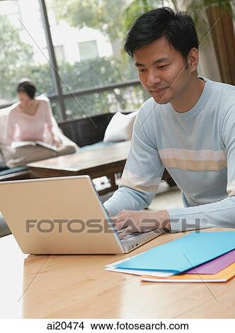 Couple at home, man using laptop, woman in background View Large Photo Image Picture - Couple at home, man using laptop, woman in background. Fotosearch
