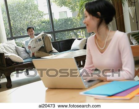 Couple at home, woman using laptop, man reading newspaper View Large Photo Image Stock Image - Couple at home, woman using laptop, man reading newspaper. Fotosearch