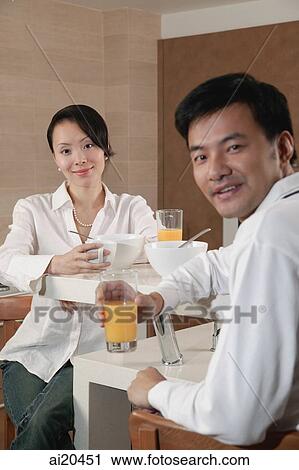 Stock Image - Couple in kitchen having breakfast, looking at camera. Fotosearch
