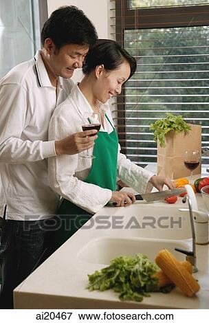 Couple in kitchen, woman chopping vegetables, man standing next to her, holding wine glass View Large Photo Image Stock Photo - Couple in kitchen, woman chopping vegetables, man standing next to her, holding wine glass. Fotosearch