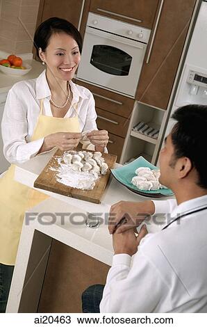Couple in kitchen, woman preparing food, man sitting, looking at her View Large Photo Image Stock Image - Couple in kitchen, woman preparing food, man sitting, looking at her. Fotosearch