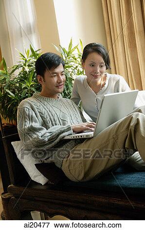 Couple in living room, looking at laptop View Large Photo Image Stock Photo - Couple in living room, looking at laptop. Fotosearch
