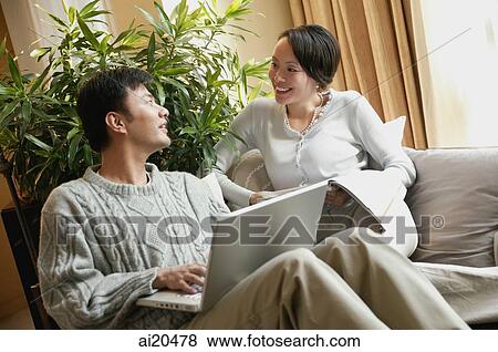 Couple in living room, man with laptop, woman holding magazine View Large Photo Image Stock Photo - Couple in living room, man with laptop, woman holding magazine. Fotosearch