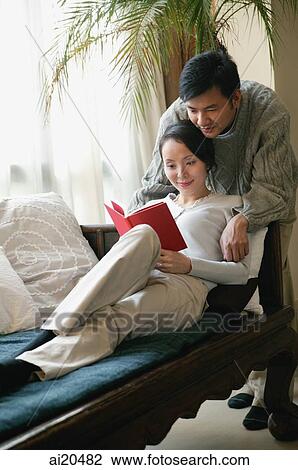 Couple in living room, woman reading a book, man leaning over her View Large Photo Image Stock Image - Couple in living room, woman reading a book, man leaning over her. Fotosearch