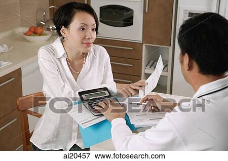 Couple sitting at kitchen table, paying bills View Large Photo Image Stock Photo - Couple sitting at kitchen table, paying bills. Fotosearch