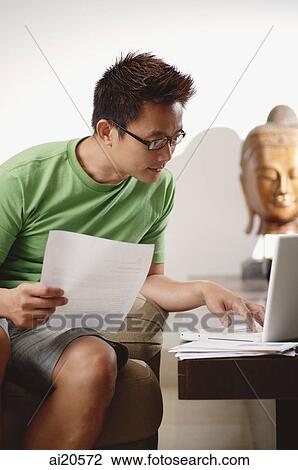 Man at home, holding documents, using laptop View Large Photo Image Stock Image - Man at home, holding documents, using laptop. Fotosearch