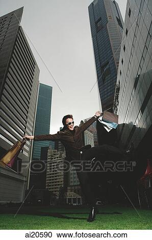 Man carrying shopping bags, jumping in mid air, buildings in the background View Large Photo Image Stock Image - Man carrying shopping bags, jumping in mid air, buildings in the background. Fotosearch