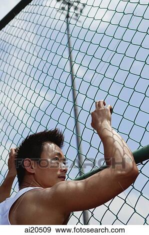 Stock Photo - Man holding on to wire mesh fence. Fotosearch