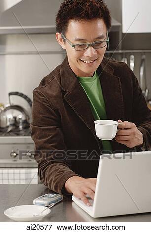 Man in kitchen, looking laptop, holding coffee cup View Large Photo Image Stock Photo - Man in kitchen, looking laptop, holding coffee cup. Fotosearch