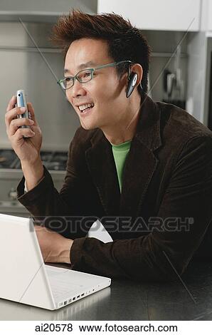 Man in kitchen, using laptop, wearing ear piece View Large Photo Image Stock Photo - Man in kitchen, using laptop, wearing ear piece. Fotosearch