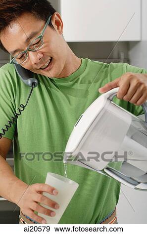 Man in kitchen, using telephone, pouring water from a jug View Large Photo Image Stock Photo - Man in kitchen, using telephone, pouring water from a jug. Fotosearch