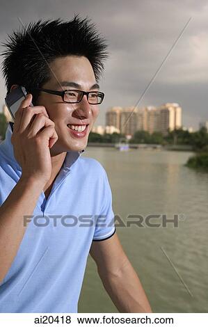 Stock Photo - Man in polo shirt and glasses, using mobile phone, lake in the background. Fotosearch