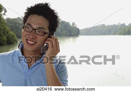 Man in polo shirt and glasses, using mobile phone, body of water in background View Large Photo Image Stock Photograph - Man in polo shirt and glasses, using mobile phone, body of water in background. Fotosearch