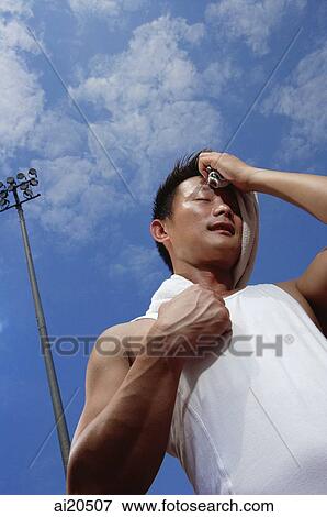 Man in sleeveless T shirt wiping his face with a towel, low angle view View Large Photo Image Stock Photo - Man in sleeveless T shirt wiping his face with a towel, low angle view. Fotosearch