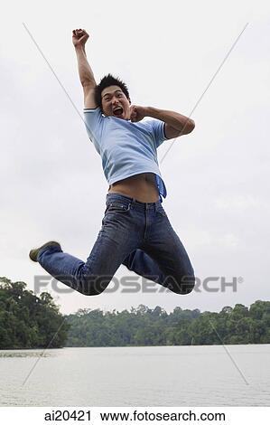 Man jumping in mid-air, arm raised, lake in the background View Large Photo Image Stock Image - Man jumping in mid-air, arm raised, lake in the background. Fotosearch