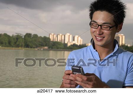 Man looking at mobile phone, body of water and buildings in the background View Large Photo Image Stock Photo - Man looking at mobile phone, body of water and buildings in the background. Fotosearch