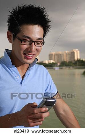 Stock Photo - Man looking at mobile phone, lake and buildings in the background. Fotosearch