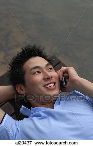 Man lying down, using mobile phone View Large Photo Image Stock Photo - Man lying down, using mobile phone. Fotosearch
