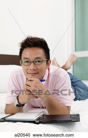 Man lying on bed, hand on chin, notebook open in front of him View Large Photo Image Stock Image - Man lying on bed, hand on chin, notebook open in front of him. Fotosearch