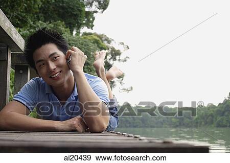 Man lying on Jetty, using mobile phone View Large Photo Image Stock Photo - Man lying on Jetty, using mobile phone. Fotosearch