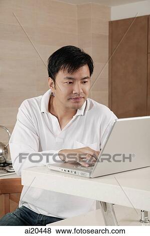 Man sitting at kitchen counter, using laptop View Large Photo Image Stock Photo - Man sitting at kitchen counter, using laptop. Fotosearch
