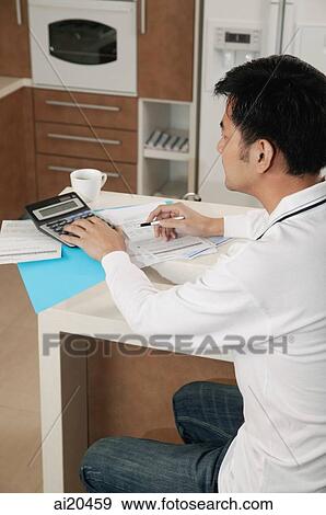 Man sitting at kitchen counter with calculator and bills View Large Photo Image Stock Photo - Man sitting at kitchen counter with calculator and bills. Fotosearch