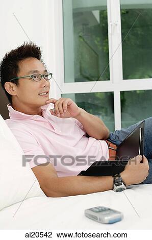 Man sitting on bed, holding notebook, hand on chin View Large Photo Image Stock Image - Man sitting on bed, holding notebook, hand on chin. Fotosearch
