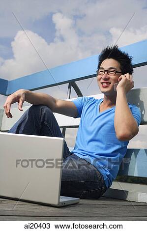 Man sitting on floor, using mobile phone, laptop in front of him View Large Photo Image Stock Image - Man sitting on floor, using mobile phone, laptop in front of him. Fotosearch