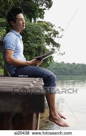 Man sitting on jetty, holding magazine, looking away View Large Photo Image Stock Photo - Man sitting on jetty, holding magazine, looking away. Fotosearch