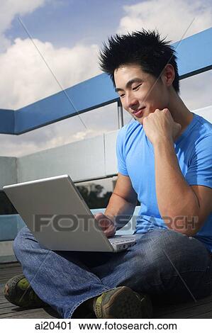 Man sitting outdoors, using laptop, hand on chin View Large Photo Image Stock Image - Man sitting outdoors, using laptop, hand on chin. Fotosearch