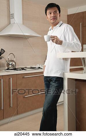 Man standing in kitchen, holding cup, looking away View Large Photo Image Stock Photography - Man standing in kitchen, holding cup, looking away. Fotosearch