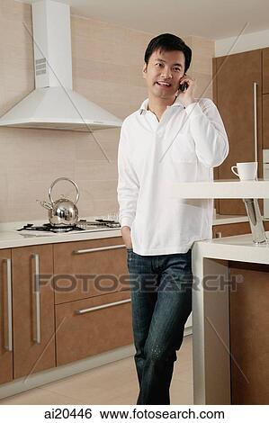 Man standing in kitchen, using mobile phone View Large Photo Image Stock Photograph - Man standing in kitchen, using mobile phone. Fotosearch
