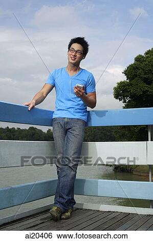 Stock Photograph - Man standing on boardwalk, listening to MP3 player. Fotosearch