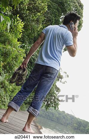 Man standing on Jetty, using mobile phone, carrying shoes in one hand View Large Photo Image Stock Image - Man standing on Jetty, using mobile phone, carrying shoes in one hand. Fotosearch