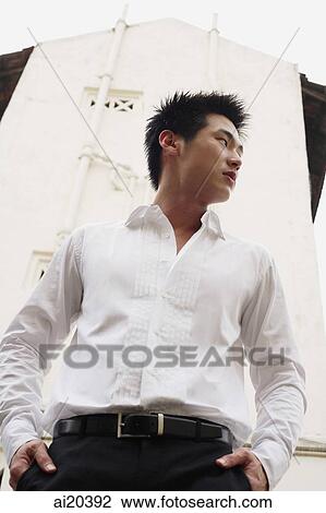 Stock Image - Man standing with hands in pockets, looking away. Fotosearch