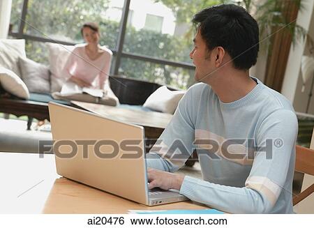 Man using laptop turning to look at woman in background View Large Photo Image Stock Photograph - Man using laptop turning to look at woman in background. Fotosearch