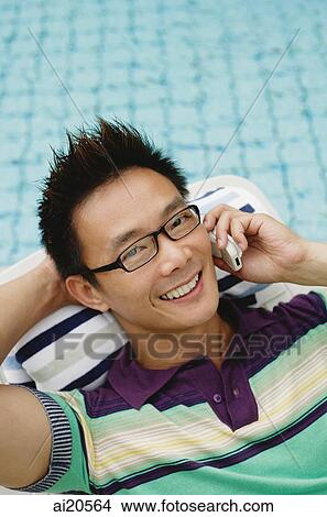 Picture - Man using mobile phone, smiling, swimming pool in the background. Fotosearch