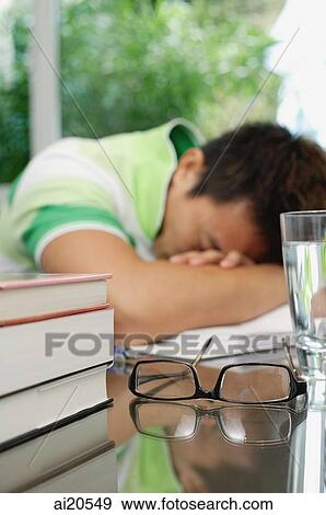 Man with head on arms, books, eyeglasses and a glass of water in the foreground View Large Photo Image Stock Photo - Man with head on arms, books, eyeglasses and a glass of water in the foreground. Fotosearch