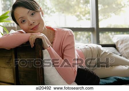 Stock Image - Portrait of a woman lying on sofa, looking at camera. Fotosearch